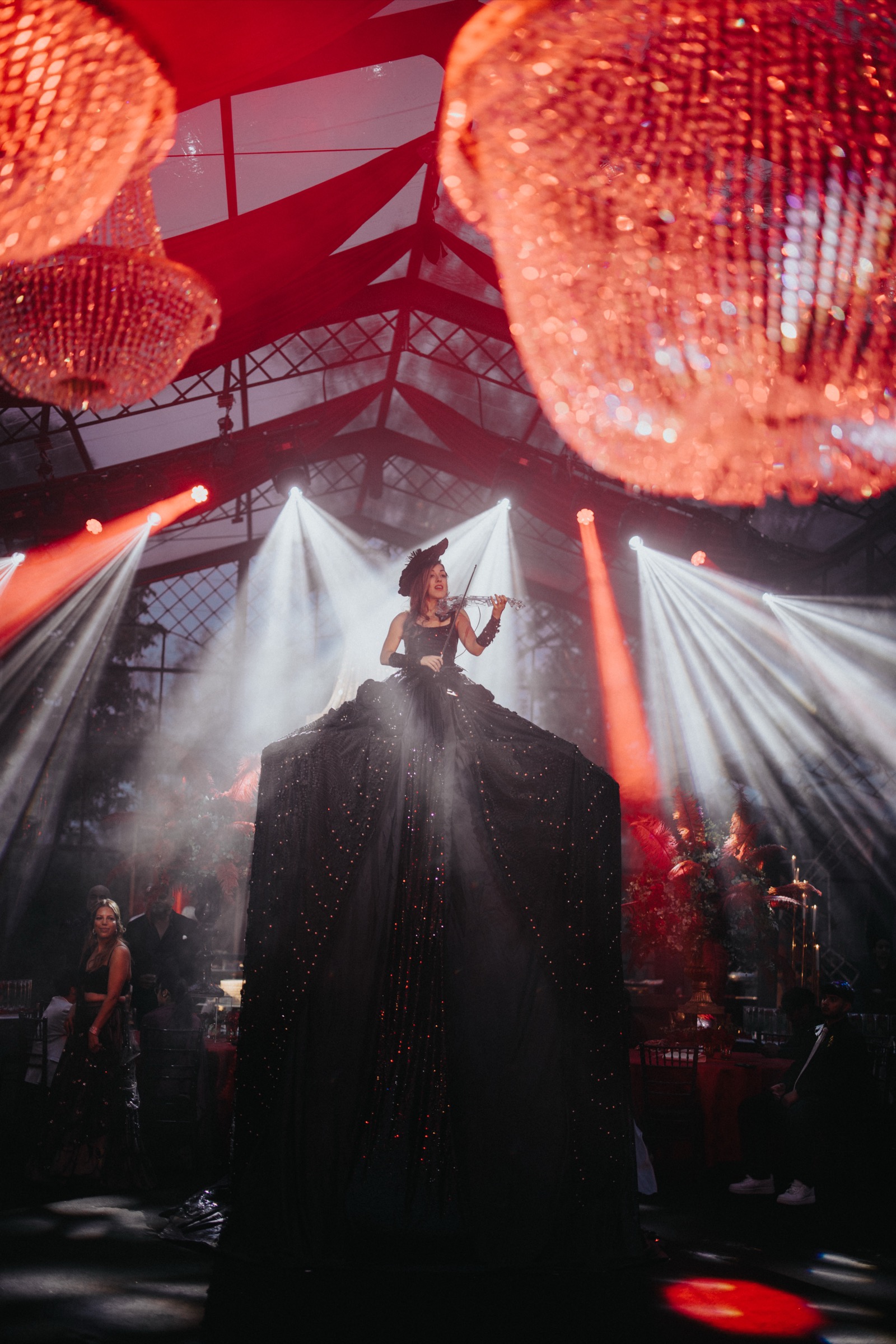 A musician playing the violin on stilts wearing a dramatic dress performing at a wedding celebration event