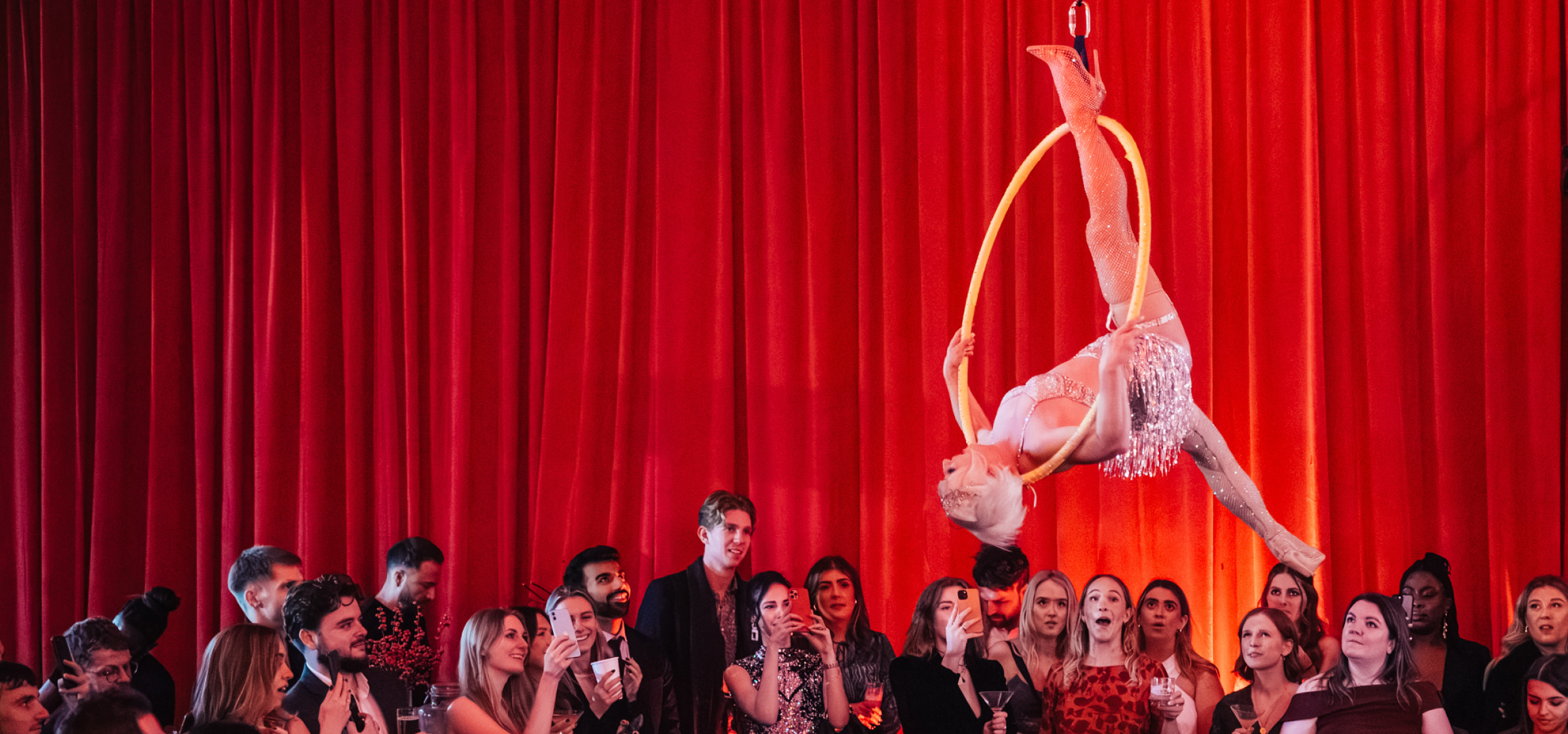An aerial performer upside down on a hoop as a amazed audience looks on